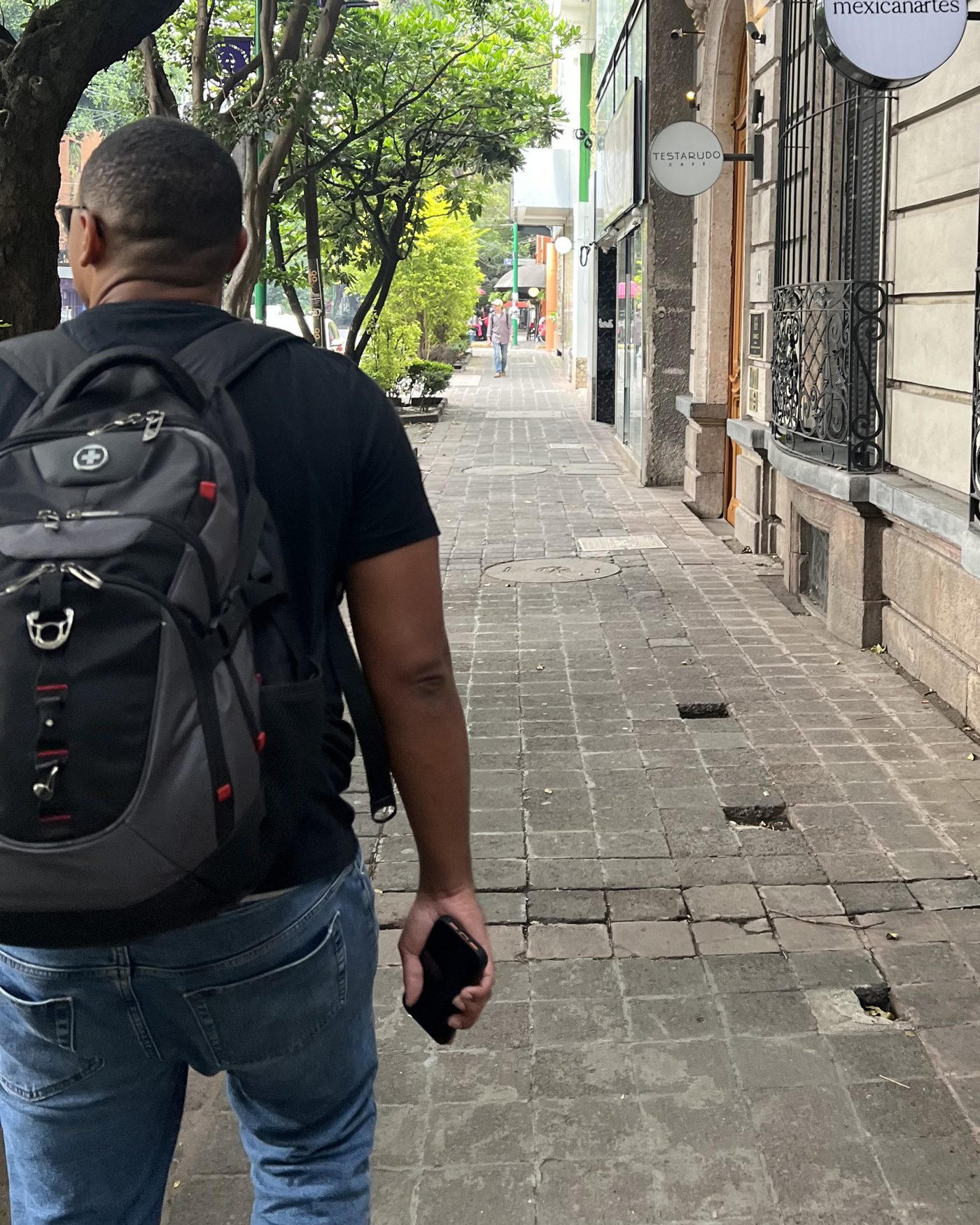 Walking a Mexico City sidewalk from behind, backpack on, phone in hand