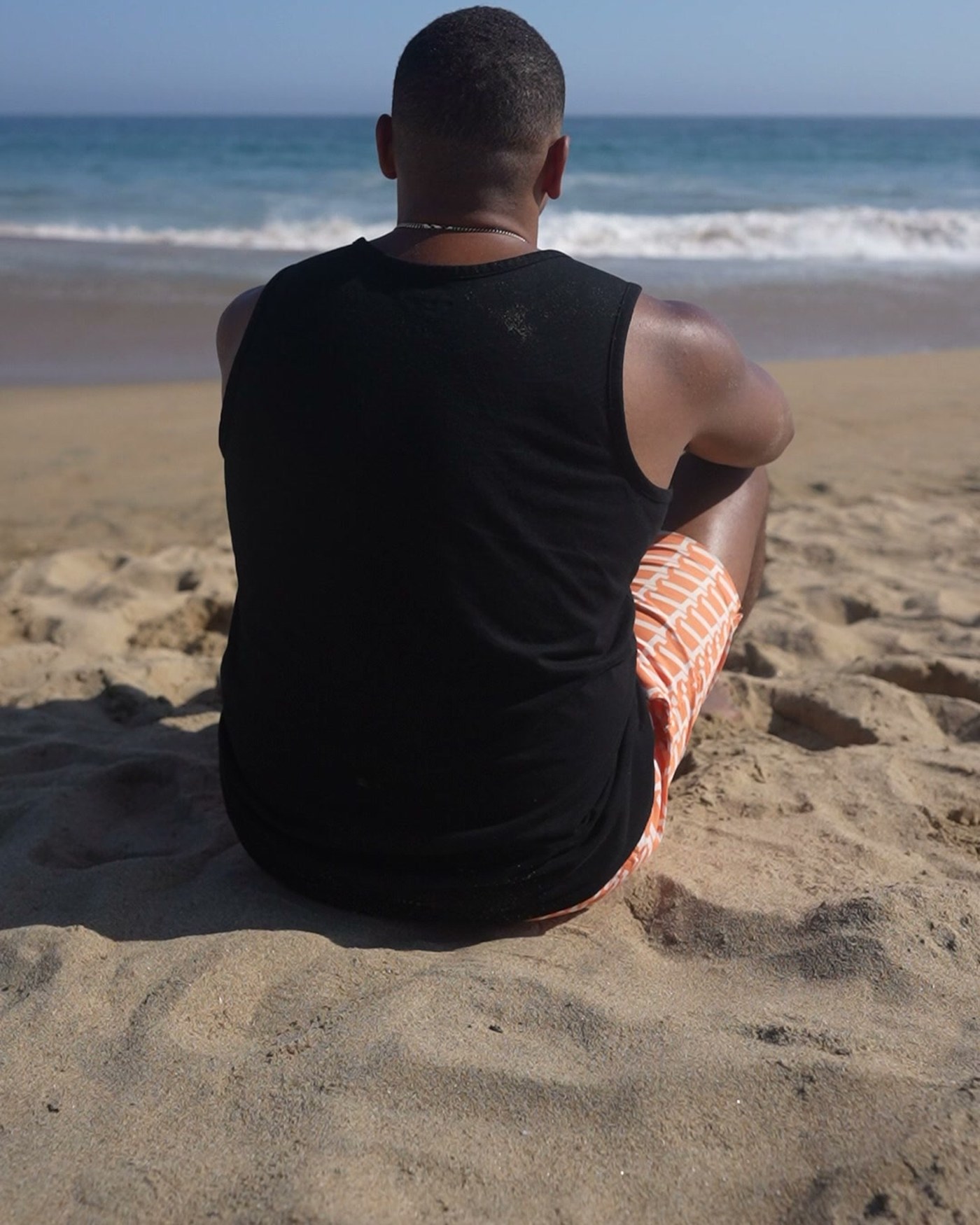 Jared Langley sitting alone in the sand, facing the ocean
