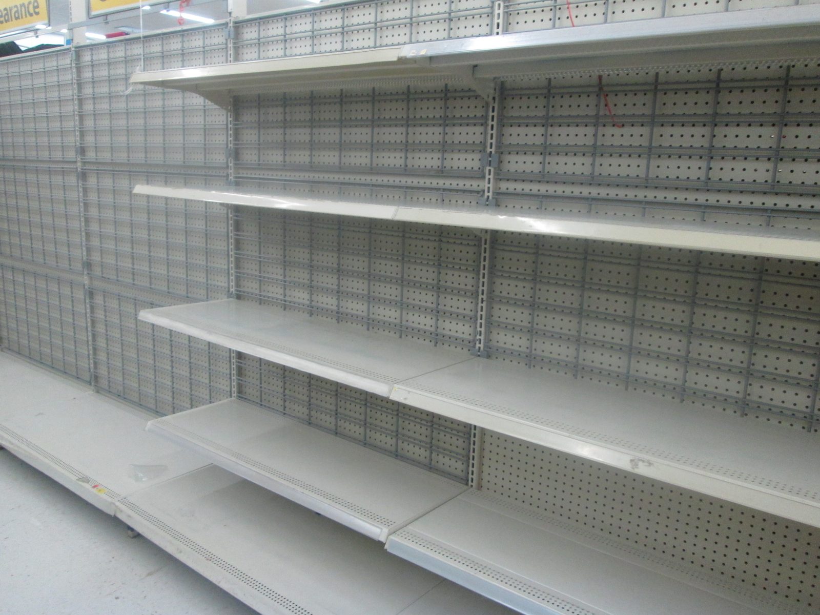 Rows of empty pegboard shelving in a retail store aisle, nothing left on any shelf